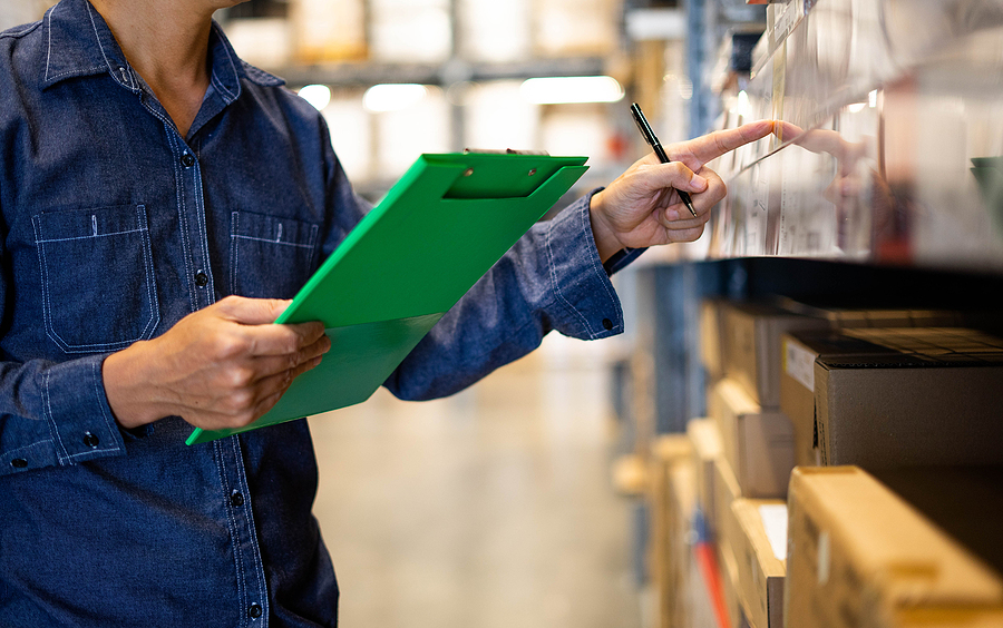 Worker doing stocktaking of product management in cardboard box on shelves in warehouse. Physical inventory count. Checking stock in factory.