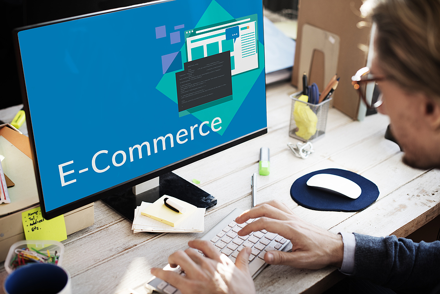 person at desk using computer. monitor has image of the words E-commerce
