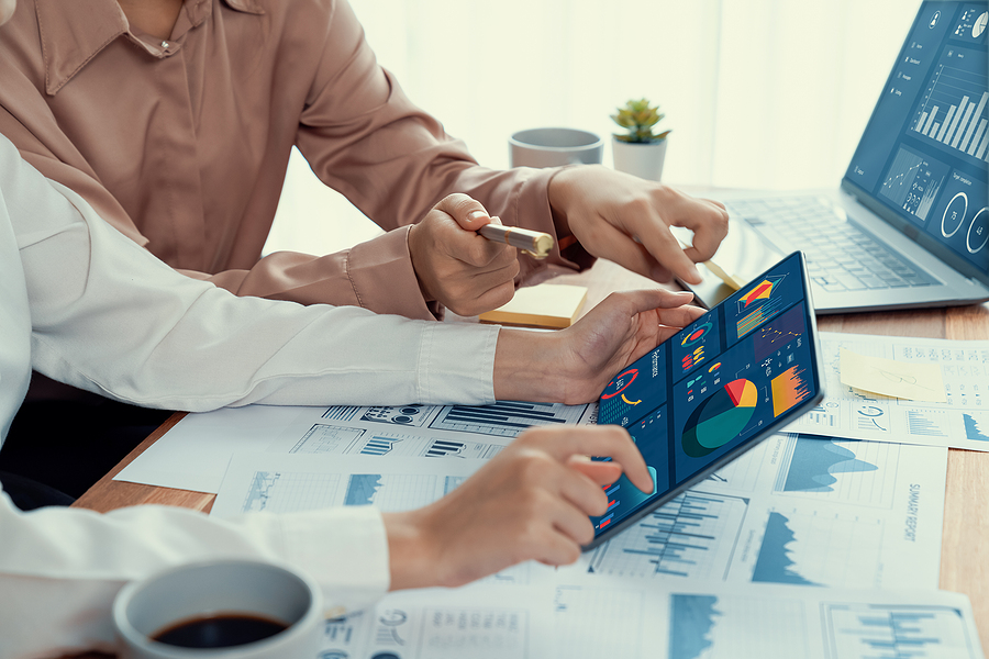 Analyst team colleague discuss financial data on digital dashboard, analyzing charts graph display on laptop and tablet screen. Modern office use business intelligence to plan marketing.